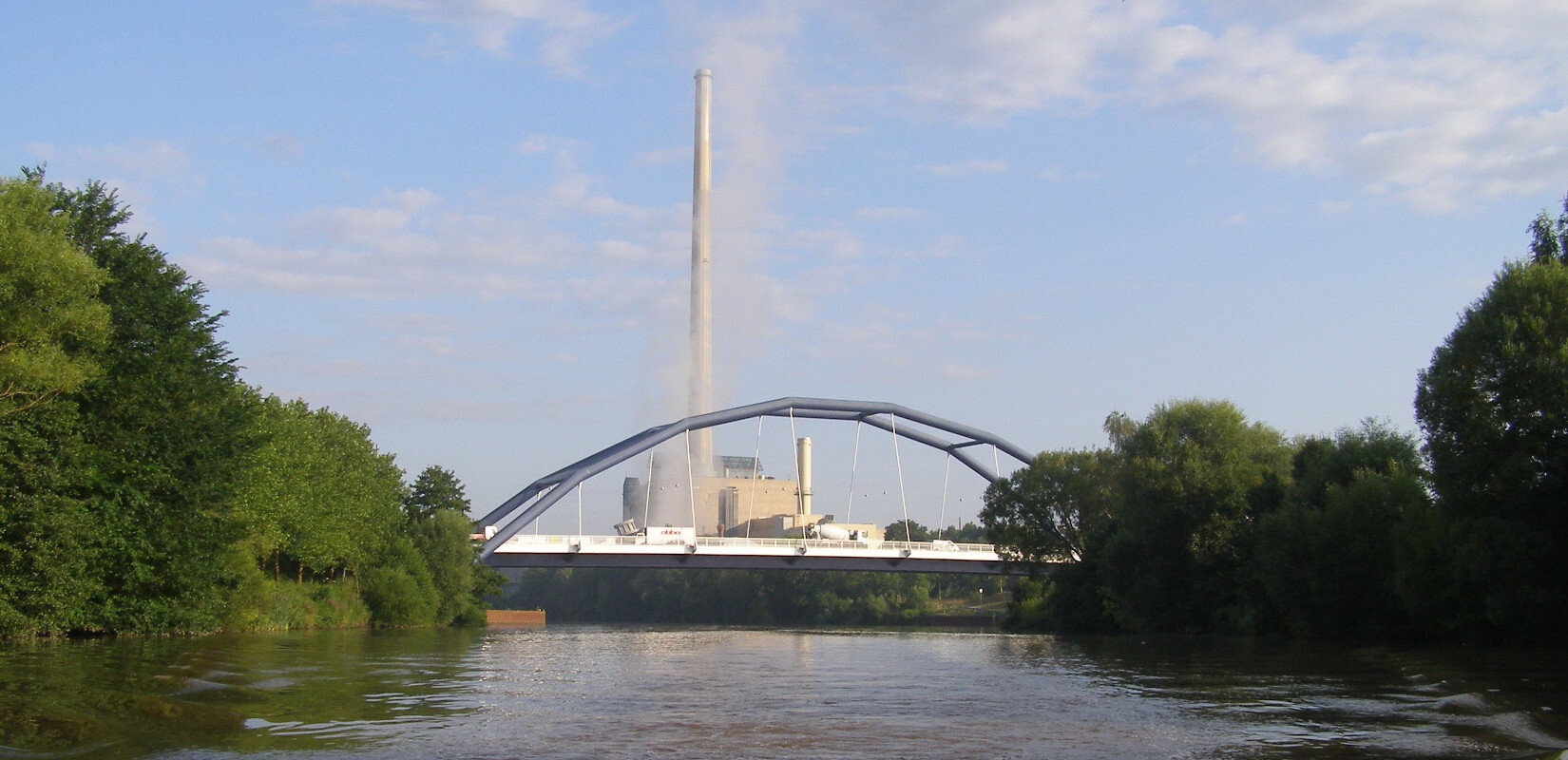 Die Saar bei Saarbrücken-Güdingen. Im Vordergrund eine Brücke über die Saar, im Hintergrund ein Industriegebäude mit hohem Schornstein.